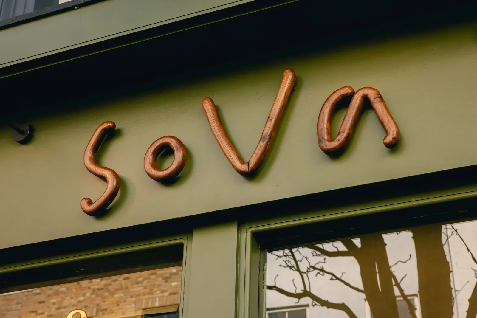 The hand-drawn sova wordmark in terracotta above the olive facade.