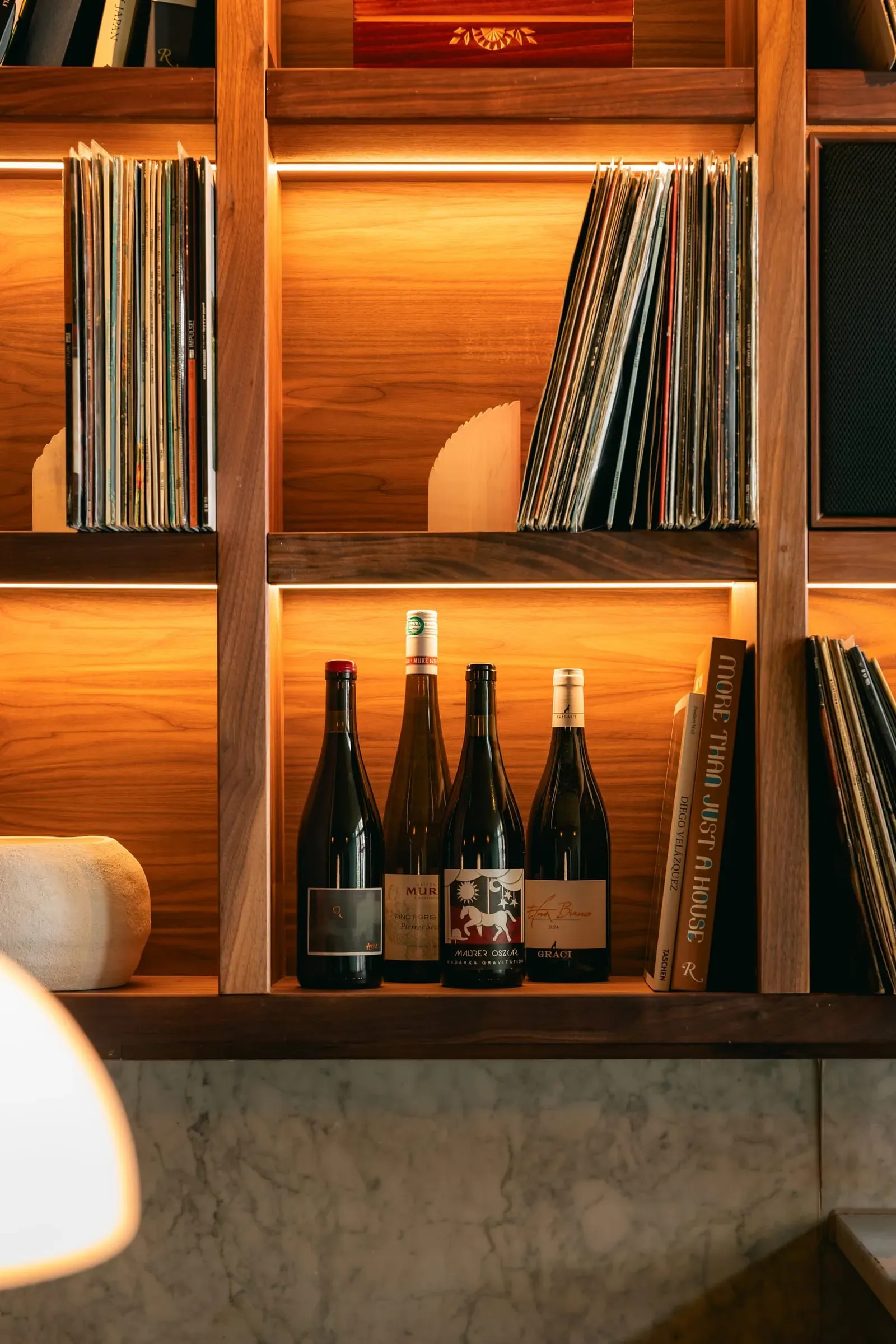 Four bottles of low-intervention wine on a lit walnut shelf beside filed records.